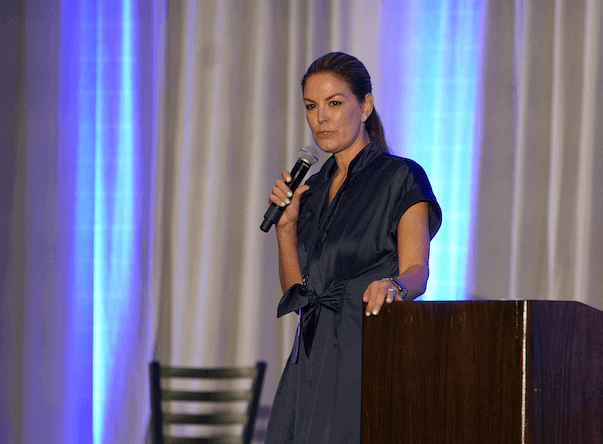 A woman in a blue dress stands at a podium, poised to speak, embodying confidence and authority in her presentation.